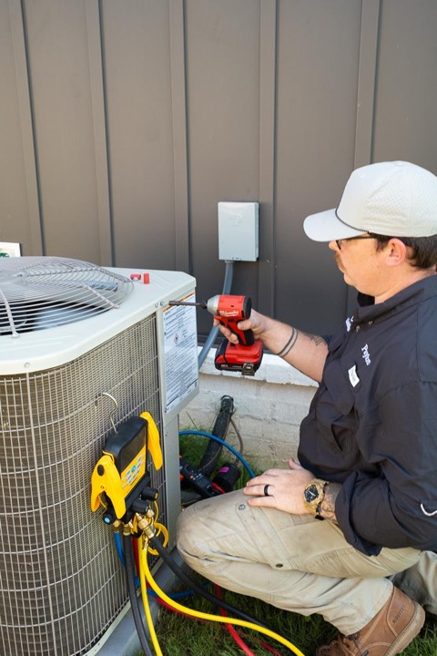 Clark technician repairing an AC condenser with a drill